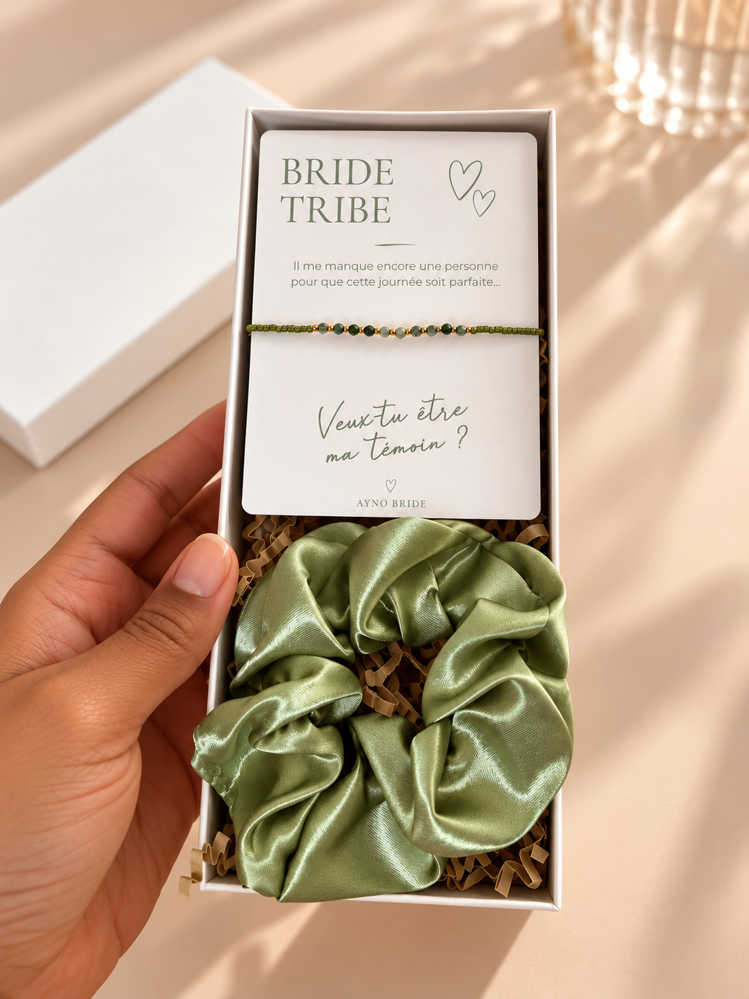 Coffret demande de témoin AYNO Bride ouvert, contenant un bracelet à perles vertes sur carte personnalisée et un chouchou en satin vert olive dans une boîte cadeau blanche.