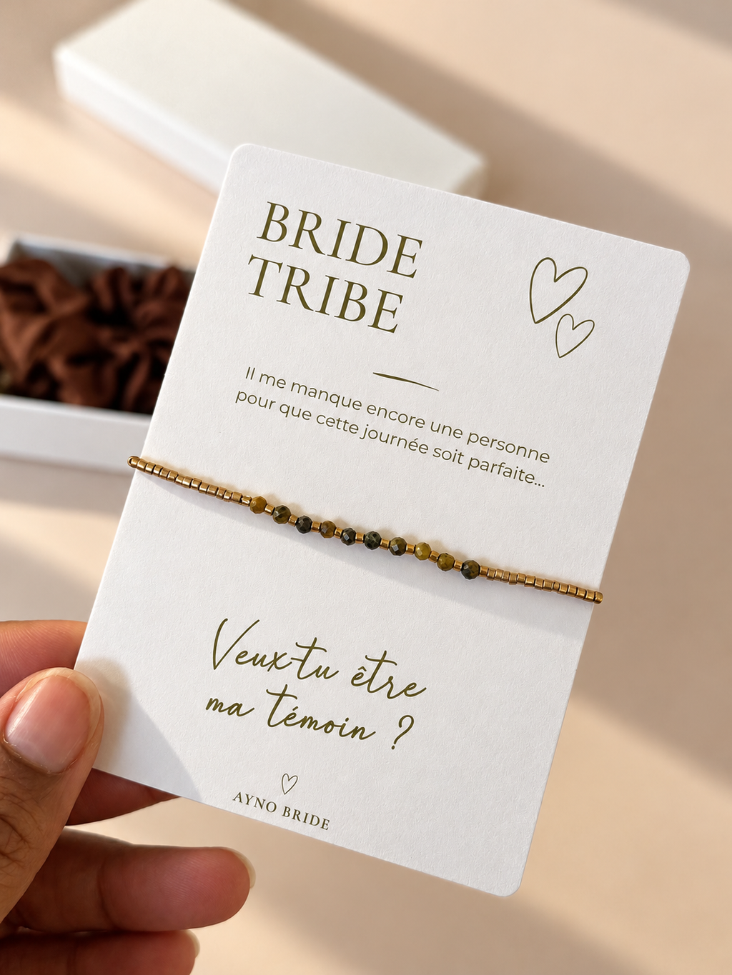 Carte de demande de témoin AYNO Bride avec bracelet à perles dorées et marron, message « Veux-tu être ma témoin ? » et coffret cadeau en arrière-plan.