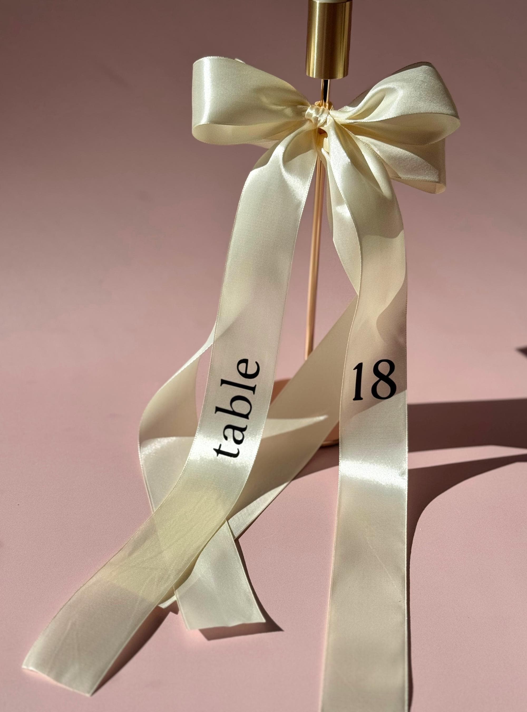Ribbon Table Number Wedding Reception Seating Arrangement Cream Satin Display Elegant Centerpiece Design Gold Hardware Detail Formal Celebration Marker Beautiful Table Decoration Customizable Text Option Luxury Event Accessory Wedding